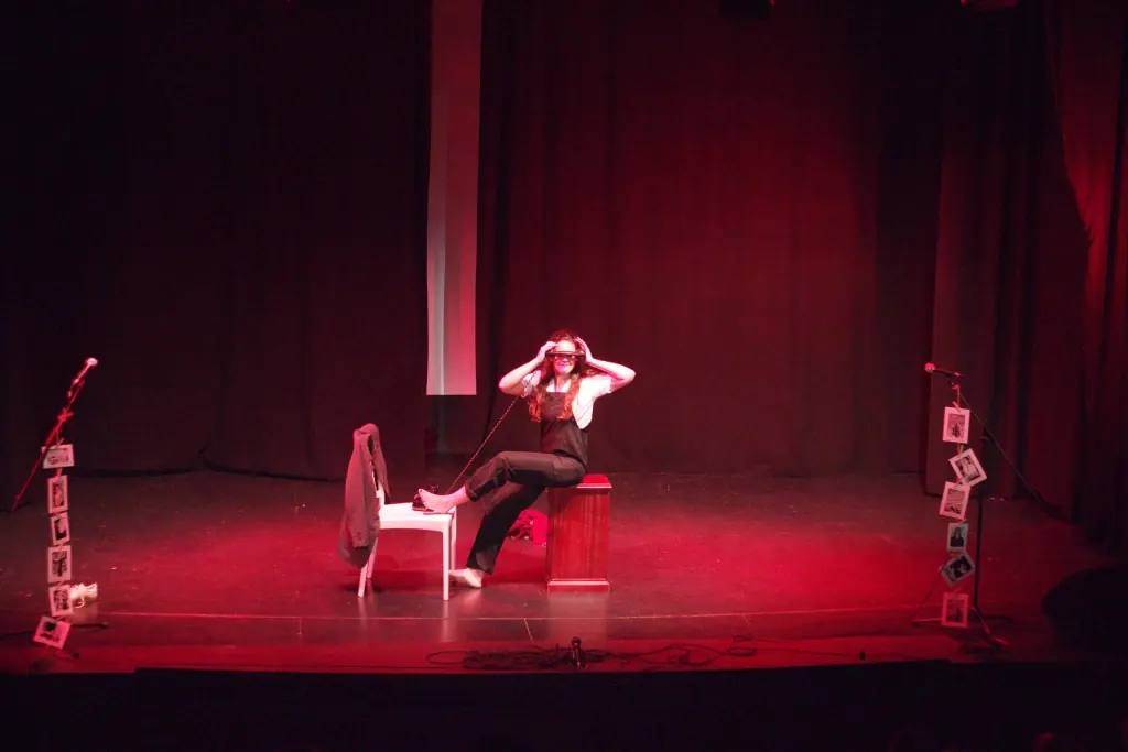 Alba Berrocal interpreta Adorando Amar, sentada junto a un teléfono en un escenario iluminado en rojo.