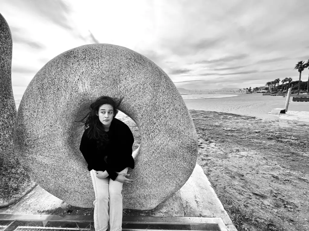 Alba Berrocal sentada dentro de una escultura circular de piedra en el paseo marítimo de Málaga, fotografía en blanco y negro