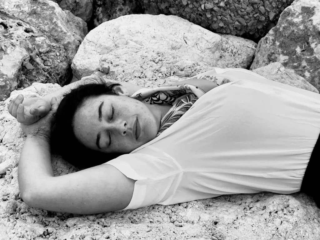 Alba Berrocal tumbada entre rocas junto al mar, con los ojos cerrados, fotografía en blanco y negro